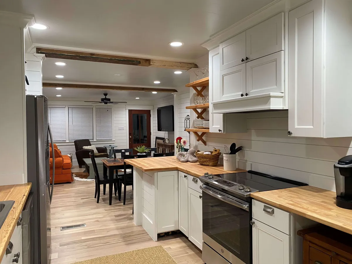 This image offers a view encompassing the kitchen island, dining table, and the living area with its signature orange couch. The layout illustrates the seamless flow between spaces, enhanced by modern, comfortable furnishings and updated finishes.