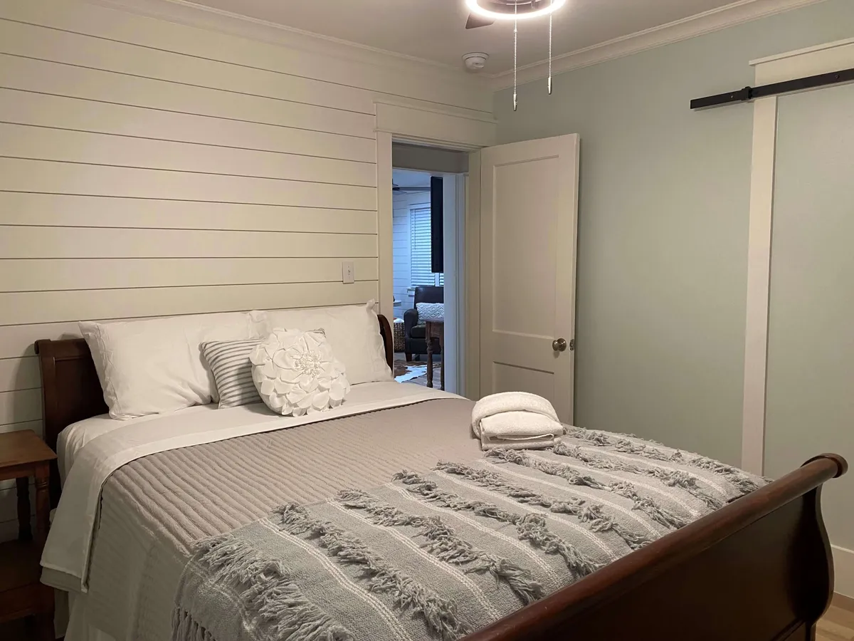 This image showcases a cozy bedroom interior, featuring a bed adorned with decorative pillows and a textured throw blanket. The doorway to another room is visible, providing a sense of openness and flow from the entry into the living spaces. The room exudes a serene, welcoming atmosphere—perfect for relaxing after a day exploring downtown or the waterfront.