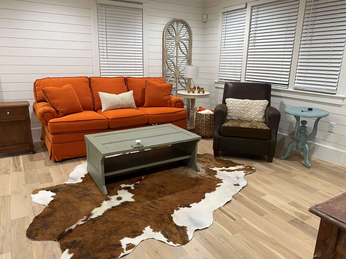 The hero image shows a beautifully renovated, inviting living room featuring a vibrant orange sofa, a chic green coffee table, a stylish cowhide rug, and a cozy brown armchair with a patterned cushion. The space feels warm and welcoming, perfect for relaxing, socializing, or unwinding with a good book.